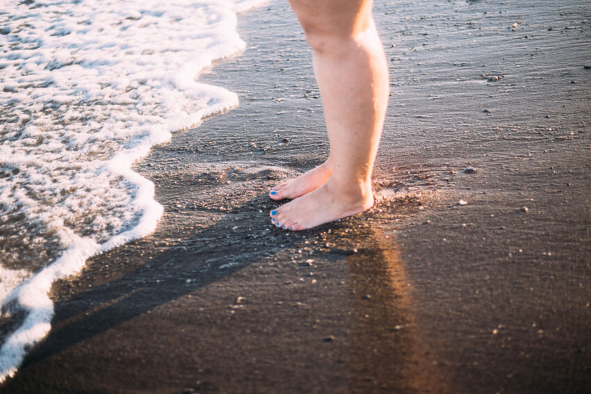 na zdjęciu: kobieta z obrzękiem nóg stoi na brzegu morza, tekst o lipodemii /fot. Getty Images