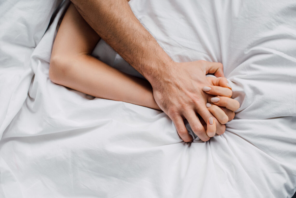 na zdjęciu: mężczyzna ściska dłoń kobiety, leżą w łóżku, tekst o tym, jak wydłużyć stosunek? /fot. Adobe Stock