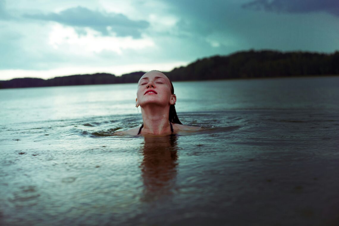 na zdjęciu: kobieta pływa w jeziorze z głową nad wodą, tekst o zaletach pływania /fot. Sarka Jonasova, Unsplash