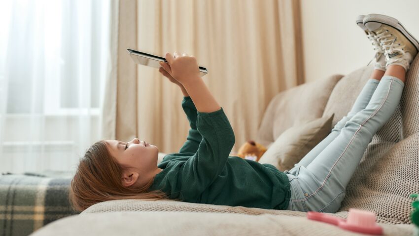 Dziecko leży na łóżku z tabletem w rękach