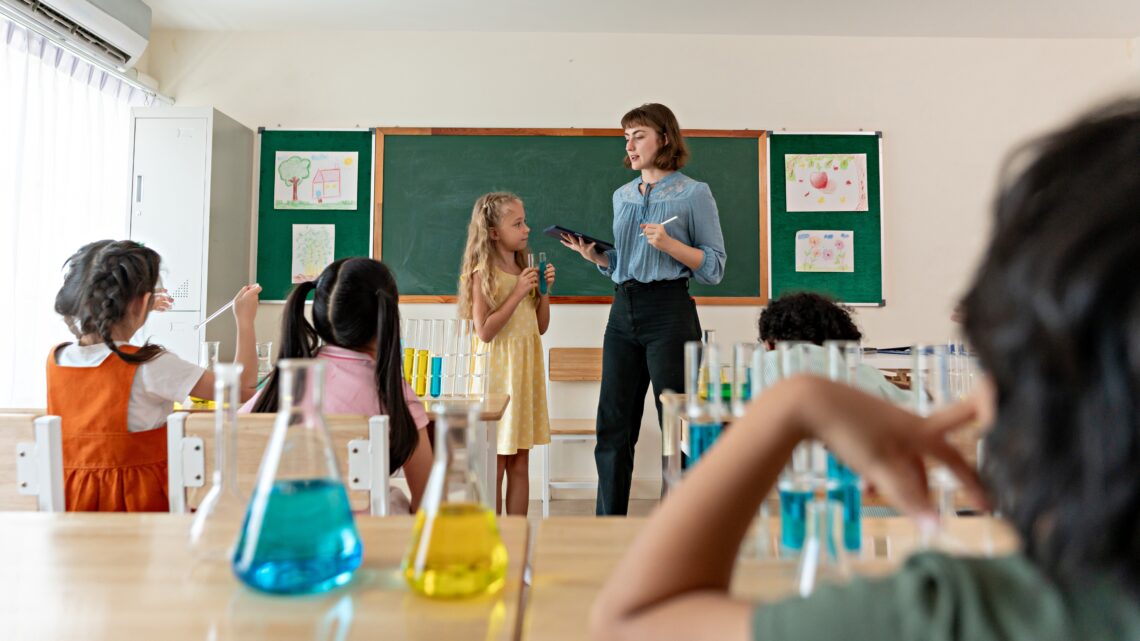 Nauczycielka wraz z uczniami w trakcie lekcji chemii, tekst o zmianach w polskich szkołach