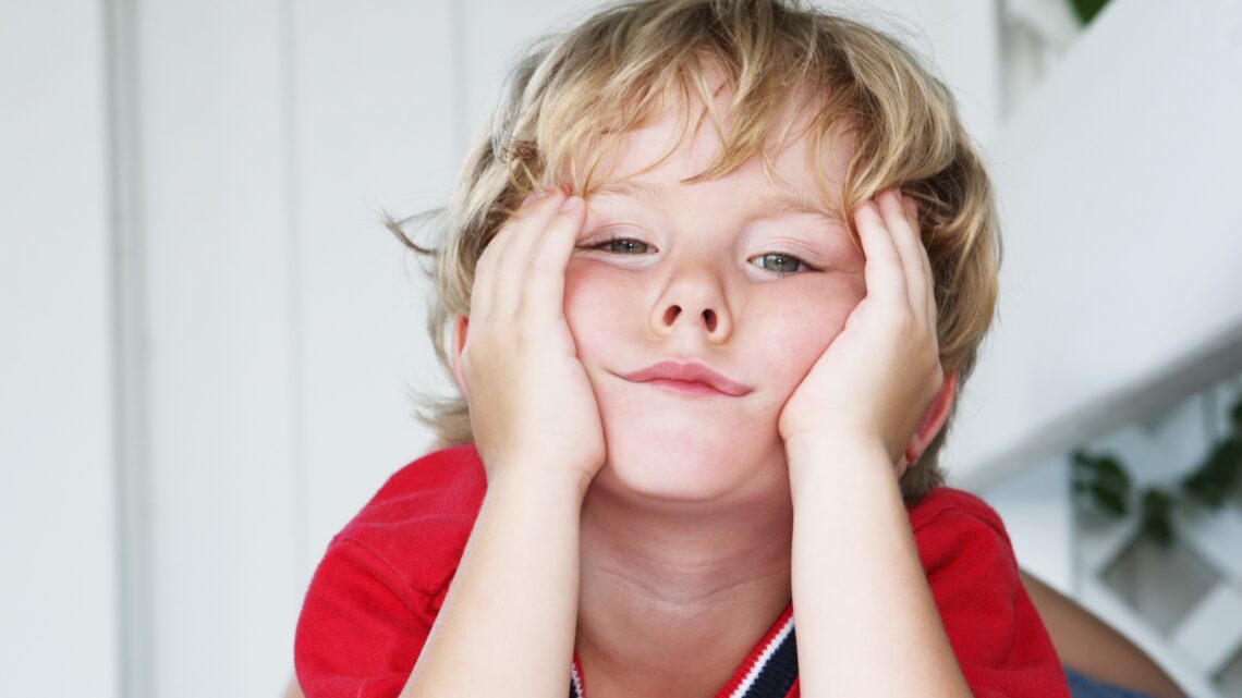 Chłopiec siedzi znudzony, opiera głowę na rękach. ADHD u dzieci może objawiać się trudnościami z koncentracją, impulsywnością oraz nadmierną potrzebą ruchu, co wpływa na funkcjonowanie w szkole i codziennym życiu.