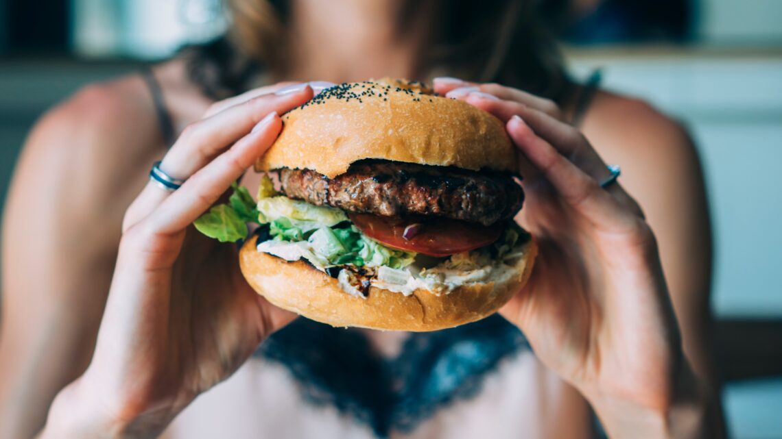 kobieta trzyma w rękach hamburgera - Hello Zdrowie