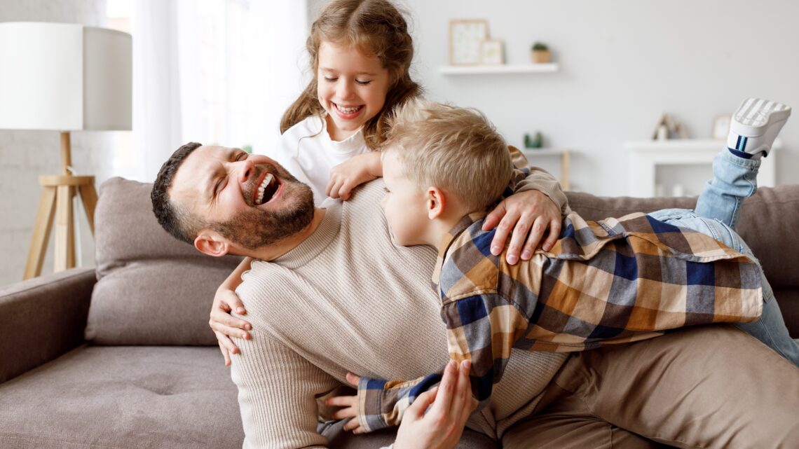 Ojciec bawi się z dziećmi na sofie, spędzając z nimi czas. ADHD ma silny komponent genetyczny i często występuje w rodzinach, co sugeruje, że może być dziedziczne.