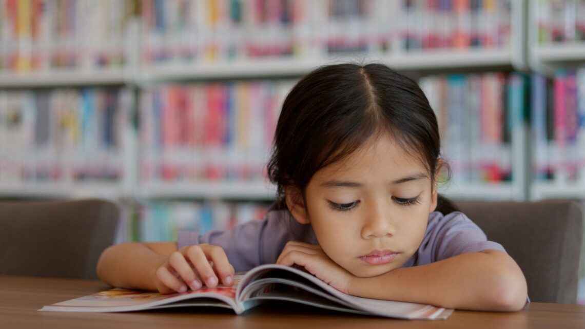 Dziewczynka czyta książkę w bibliotece. Wygląda na znudzoną. Diagnoza ADHD obejmuje ocenę trudności z koncentracją, impulsywnością i nadmierną aktywnością poprzez wywiad, obserwację oraz specjalistyczne testy.