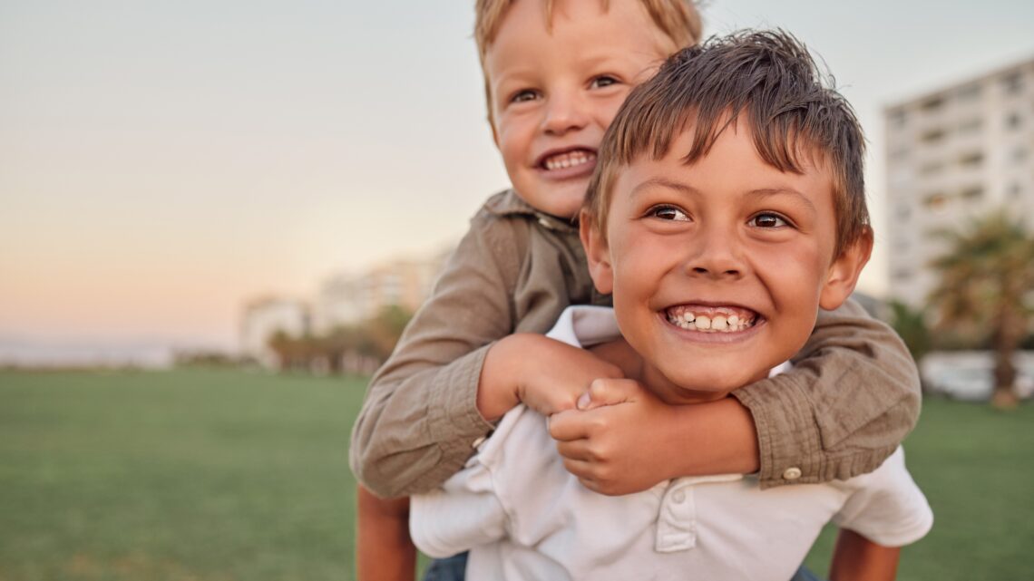 Dwaj bracia bawią się na świeżym powietrzu, śmiejąc się i ciesząc wspólną zabawą. ADHD u dzieci w wieku przedszkolnym często objawia się nadmierną ruchliwością, trudnościami ze skupieniem uwagi, impulsywnością oraz problemami z przestrzeganiem zasad i regulacją emocji.