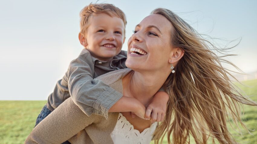 Mama nosi dziecko na plecach, oboje śmieją się i cieszą wspólną zabawą. Wyróżnia się trzy główne rodzaje ADHD: przewagę zaburzeń uwagi, przewagę nadpobudliwości i impulsywności oraz typ mieszany, który łączy obie cechy, wpływając na codzienne funkcjonowanie.